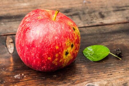 A red ripe apple with pear leaf on the wooden background