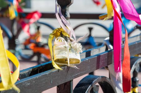 A closed wedding padlock covered by white tulle and decorated with artificial flower and ribbons on the black metal fenceの写真素材