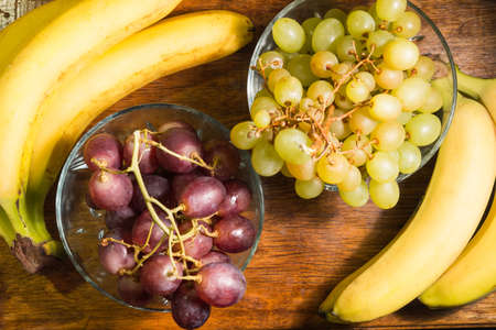 A top view at the bananas and grapes on the wooden backgroundの写真素材
