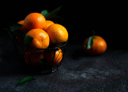 Mandarins with green leaves. Bright orange tangerines with leaves lie in a basket on a dark background. Dark photo. The photo shows a textured backgroundの写真素材