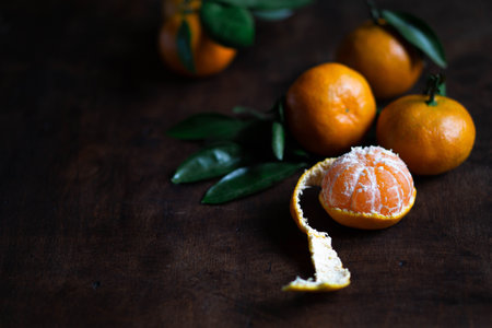 Mandarins with green leaves. Some orange tangerines with leaves lie on a dark wood textured surface. One of the tangerines is peeled. Selective focus. Dark photo. Copy spaseの写真素材