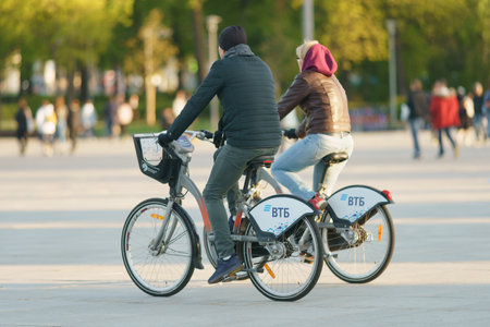 Moscow, Russia - May 23, 2022: Pair of young man and woman cycling in the Moscow city public park in the spring sunny day. Healthy lifestyle concept. Backs, rear viewのeditorial素材