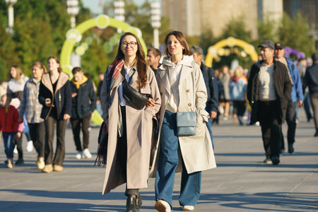 Moscow, Russia - September 10, 2022: Street photography. Youth on the city street in the day. lifestyle concept. Portraits of happy friends. One of them use smartphone. both glowing with happinessのeditorial素材