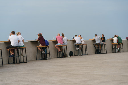 Svetlogorsk, Kaliningrad reg., Russia - August 20, 2022: Photography of beautiful people of different generations sitting in outdoor cafe in front of the Baltic sea. Blue sky as background. back viewのeditorial素材