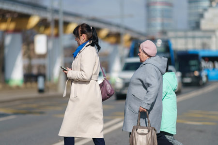 Moscow, Russia - March 28, 2023: People on the city street in the sunny spring day. Young and senior women wait for green light of stop light to cross the street. Spring fashion. Street photographyのeditorial素材
