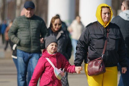 Moscow, Russia - March 28, 2023: People on the city street in the sunny spring day. Mother leads daughter by the hand. Modern lifestyle concept and spring fashion. Street photography. Front viewのeditorial素材
