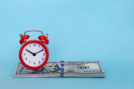 The alarm clock stands on a stack of money on a blue backgroundの写真素材