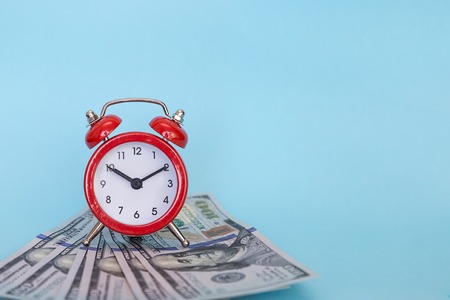 The alarm clock stands on a stack of money on a blue backgroundの写真素材
