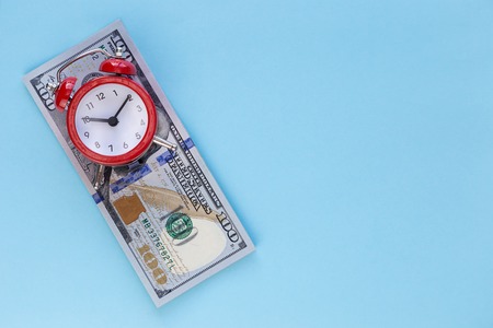 The alarm clock stands on a stack of money on a blue backgroundの写真素材