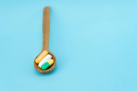 pills and capsules in a wooden spoon lie on a blue backgroundの写真素材