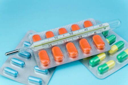 blisters with pills and thermometer lie on a blue backgroundの写真素材