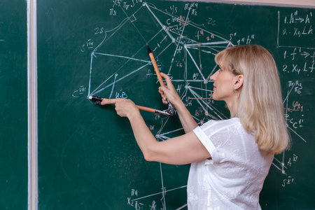 A young Caucasian female math teacher stands at the blackboard and explains the solution of a mathematical problemの写真素材
