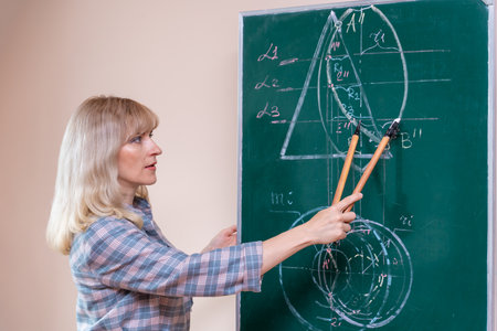 A young Caucasian female math teacher stands at the blackboard and explains the solution of a mathematical problemの写真素材