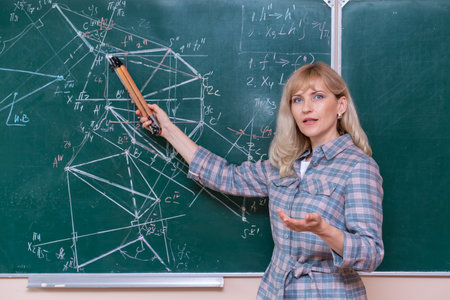 A young Caucasian female math teacher stands at the blackboard and explains the solution of a mathematical problemの写真素材