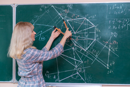 A young Caucasian female math teacher stands at the blackboard and explains the solution of a mathematical problemの写真素材