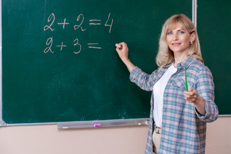 A young Caucasian female math teacher stands at the blackboard and explains the solution of a mathematical problemの写真素材