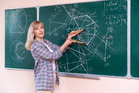A young Caucasian female math teacher stands at the blackboard and explains the solution of a mathematical problemの写真素材