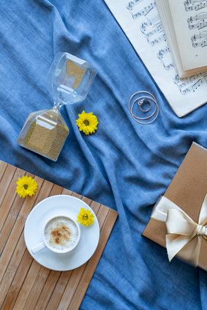 A cup of coffee, an hourglass of music notes and a box of chocolates are laid out on a blue backgroundの写真素材