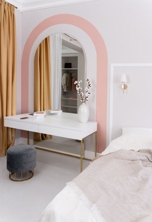 Modern bedroom with a white desk and arched mirror. Room is decorated a vase of flowers and booksの写真素材