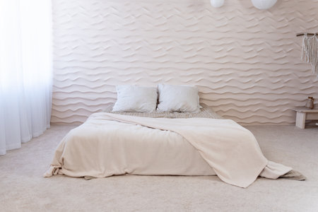 Minimalist bedroom with unique wavy wall design, illuminated by natural light from the side windowの写真素材