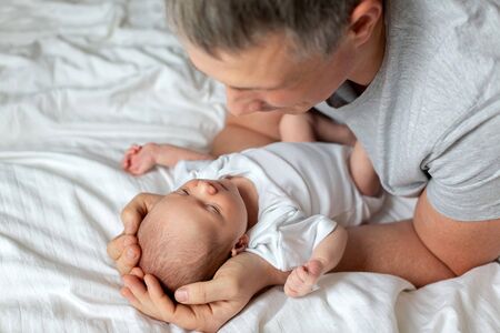 A newborn baby in the arms of the Pope on a white sheet on the bed. Cute newborn baby with father....