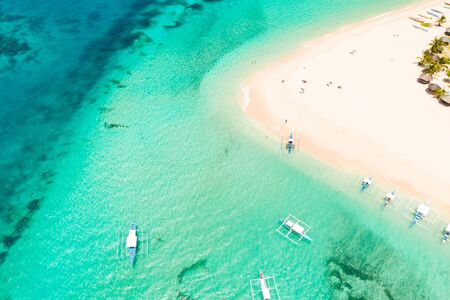 Daco island, Philippines. Palm trees and bungalows on the white sandy beach. People relax on a...