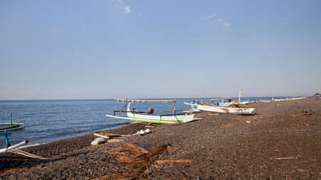 Fishing boats on the beach of Bali island. Sea and black volcanic sand. Seascape in sunny weather.