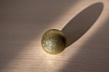 Glitter christmas ball. Golden sphere, abstract decoration. Shiny ball on the table, sunlight.の写真素材