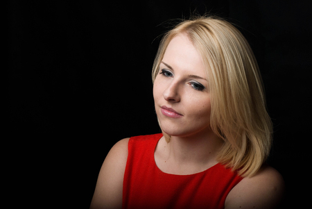 Photo of the girl of the blonde in a red dress with a thoughtful look. Black background.の写真素材