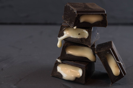 Chocolate pieces with creamy liquid vanilla filling. Dark background.