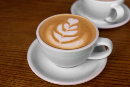 Two cups of coffee on the wooden table in the cafe. Light cup of cappuccino.