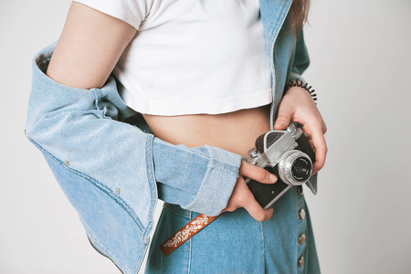 The girl's body on a white copyspace background in photo Studio, face off. Holds a retro camera. Wearing a denim suit. Denim long skirt and jacket. Nostalgia 90's.の写真素材