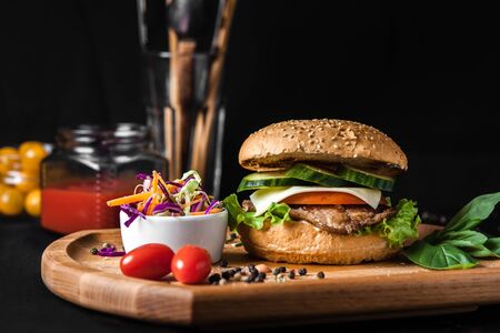 Fish burger with on wooden Board for take away with cabbage salad. On black background.の写真素材