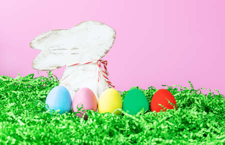 background an easter with a figurine of a rabbit with colored eggs in the grass on a pink...