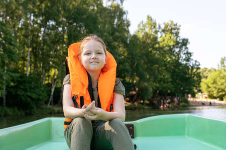 little girl in a life jacket rides a boat in the summer against the background of the forestの写真素材