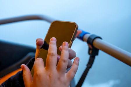 a child holds a phone, a smartphone in his hands during an extreme trip on a cable car, uses a mobile application, close-upの写真素材