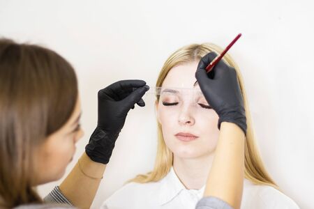 Female cosmetologist performs eyebrow correction on beautiful models in the beauty parlor. The girls face is a blonde. Close-up. Facial careの写真素材