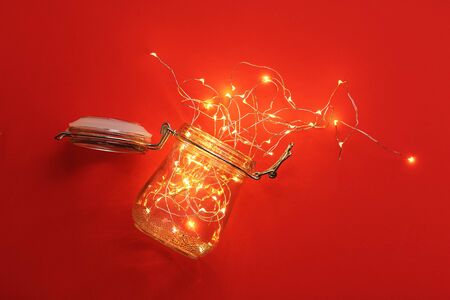Garland inside a jar with a yoke. Red background and warm light, christmas mood. Minimalism and a classic combination of colors. New Year's greetings. Xmas bang.の写真素材