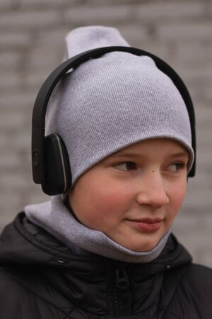 A teenager listens to music in black wireless headphones. Cool once and brick walls of houses. Modern children and technologyの写真素材