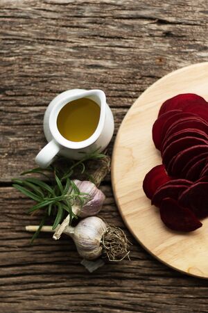 Beetroot Chips. The process of making snacks. Handmade healthy vegetable chips. On a cutting board are slices of root vegetables. Garlic and oregano spices for the dish. The preparation uses olive oil and salt. Soft focusの写真素材