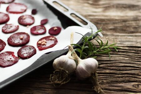 Beetroot Chips. The process of making snacks. Handmade healthy vegetable chips. On baking paper are slices of root vegetables. Garlic and oregano spices for the dish. Soft focusの写真素材