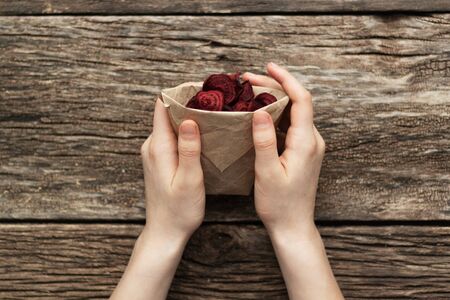 Home-made beet chips. Snacks are wrapped in a paper bag. Hand holds food bag. Handmade healthy vegetables chipsの写真素材