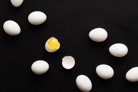 White eggs lie scattered on a black background. One egg is broken and the yolk is visible....