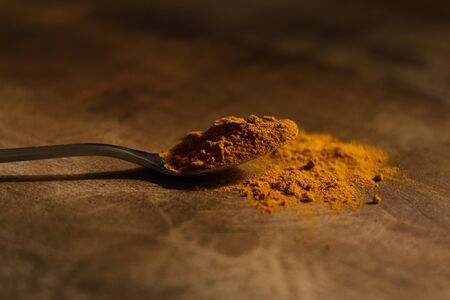 A spoonful of turmeric powder in a metal spoon. Dark wood background in warm shadesの写真素材