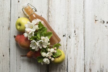 Bottle of apple and pear juice, fresh pears, apples and flowers on white woodenの写真素材