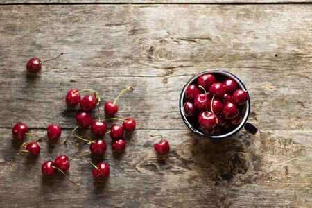 Ripe fresh sweet cherry lies in a metal old mug and on a wooden rustic table. Healthy sweet dessert.の写真素材