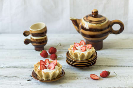 Dessert tartlets with butter cream and fresh strawberries on a white wooden background. Ceramic...