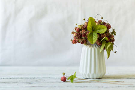 Ripe and green strawberries with leaves and flowers in a ceramic vase on a white background