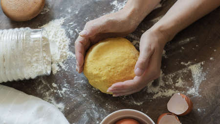 Kneading the Dough. Female hands hold homemade dough. On the table are flour, napkin, eggs and shellsの写真素材