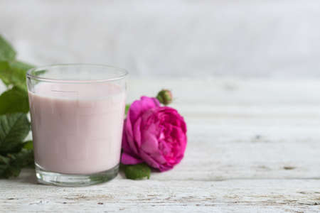 Ayurvedic drink pink milk or matcha. A glass of refreshing cocktail stands on a wooden white background. Nearby lies a lilac roseの写真素材